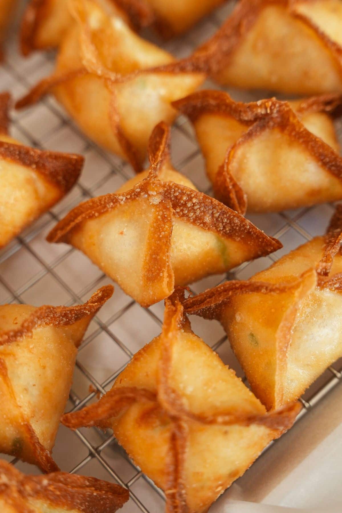 Crab rangoons resting on a wire rack after frying.