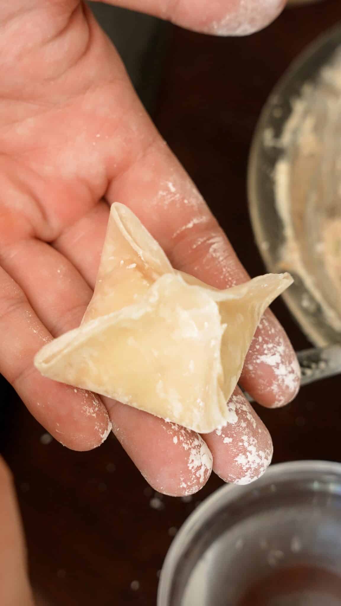 An uncooked crab rangoon folded in a hand.