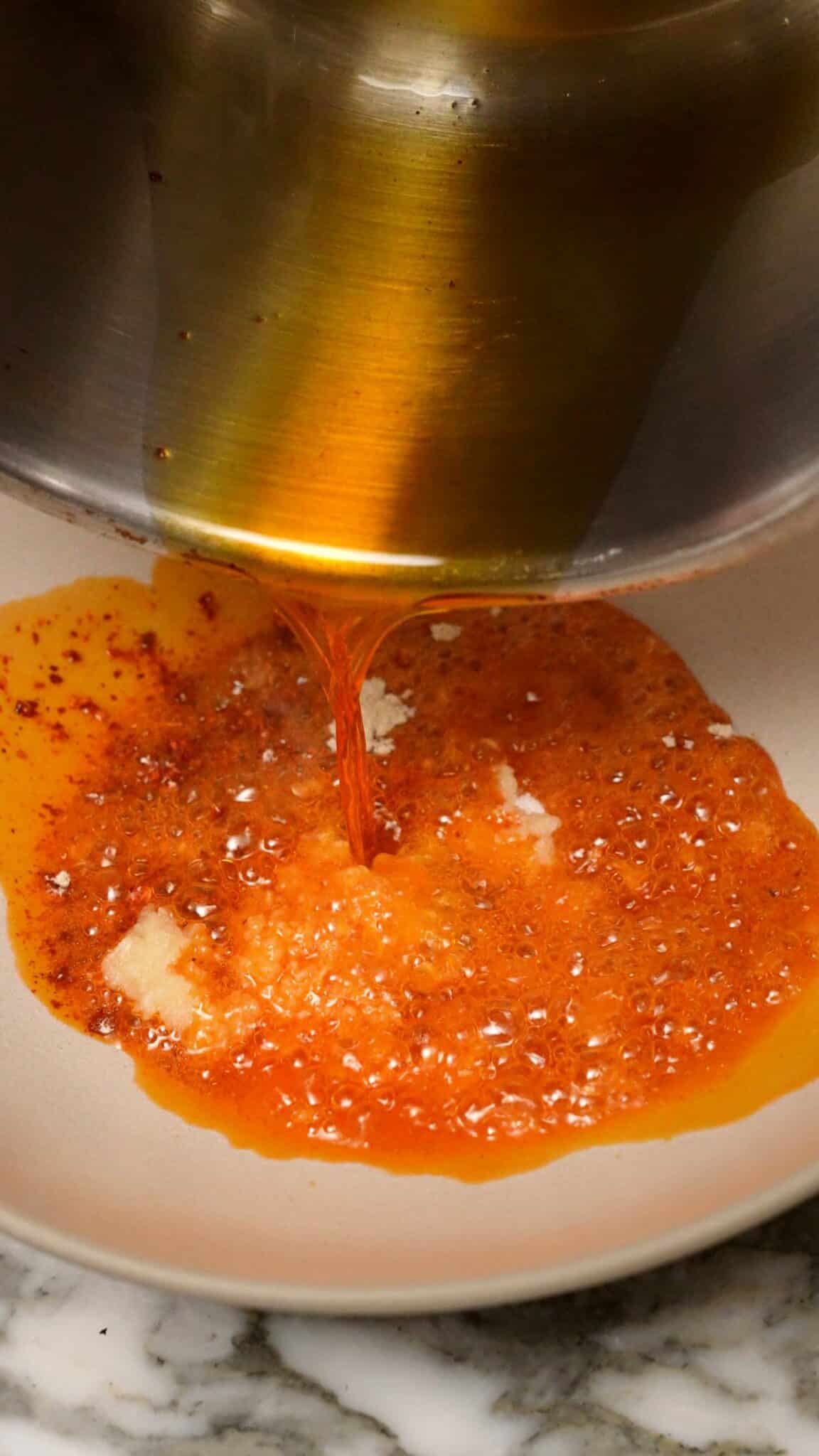 Hot oil being poured onto spices in a ceramic bowl.