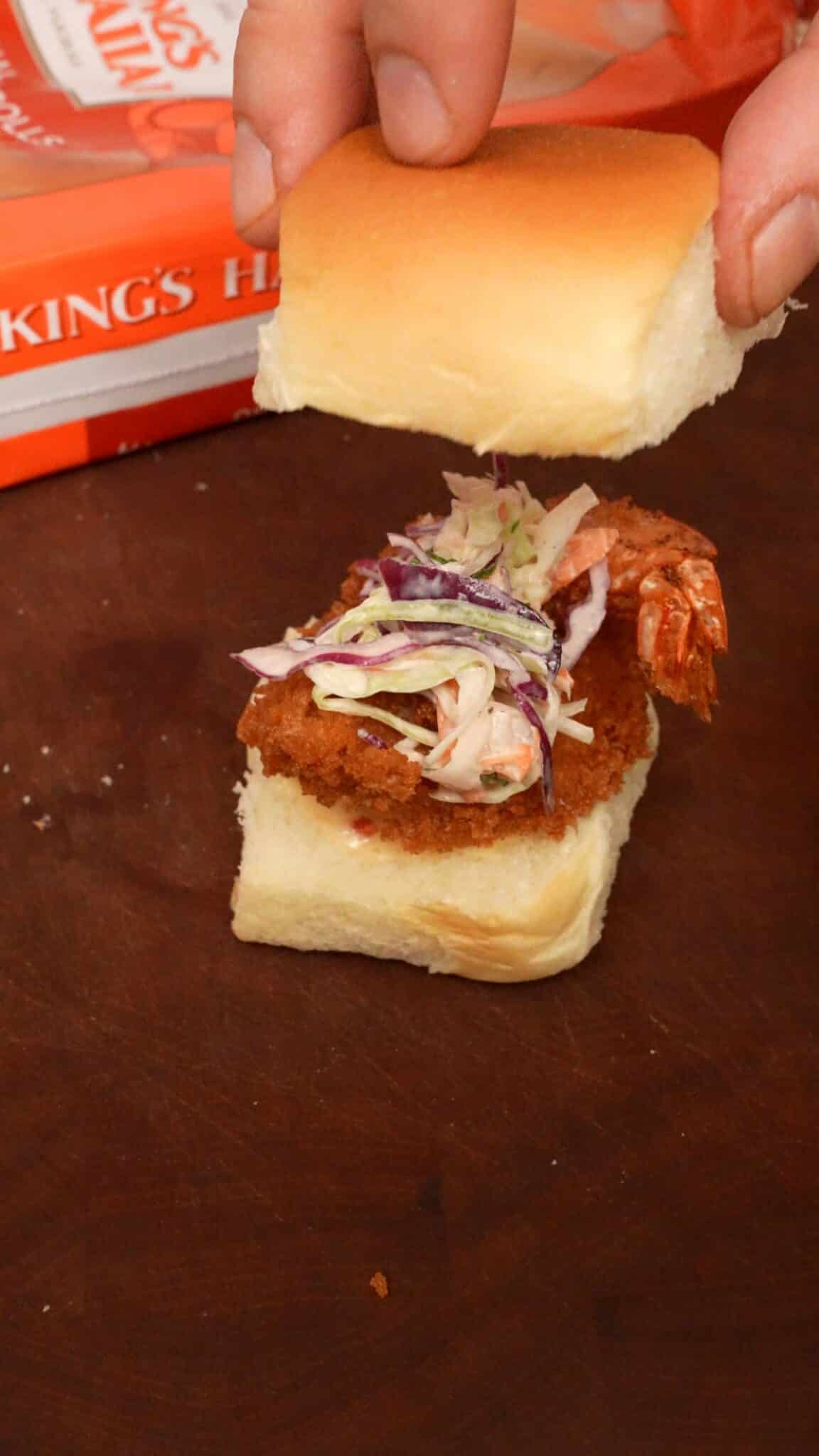 A fried shrimp slider being assembled on a cutting board.