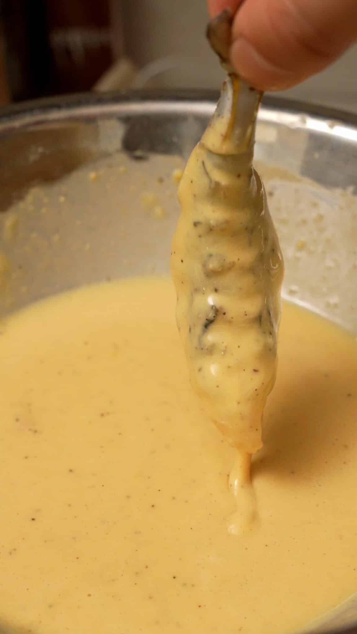 A shrimp being dredged in wet batter for Fried Shrimp sliders.