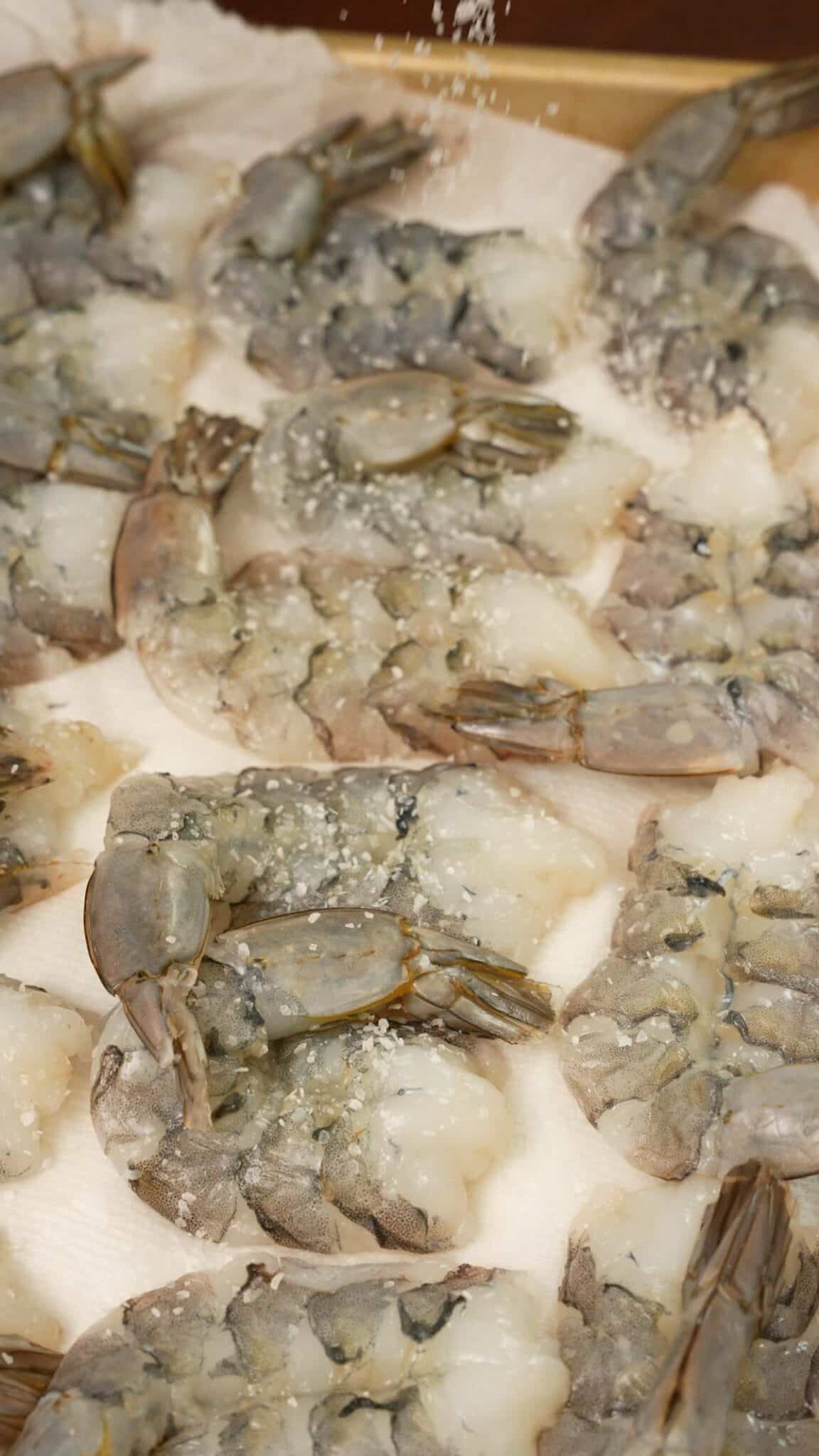 Butterflied shrimp on a paper towel lined sheet seasoned with salt.