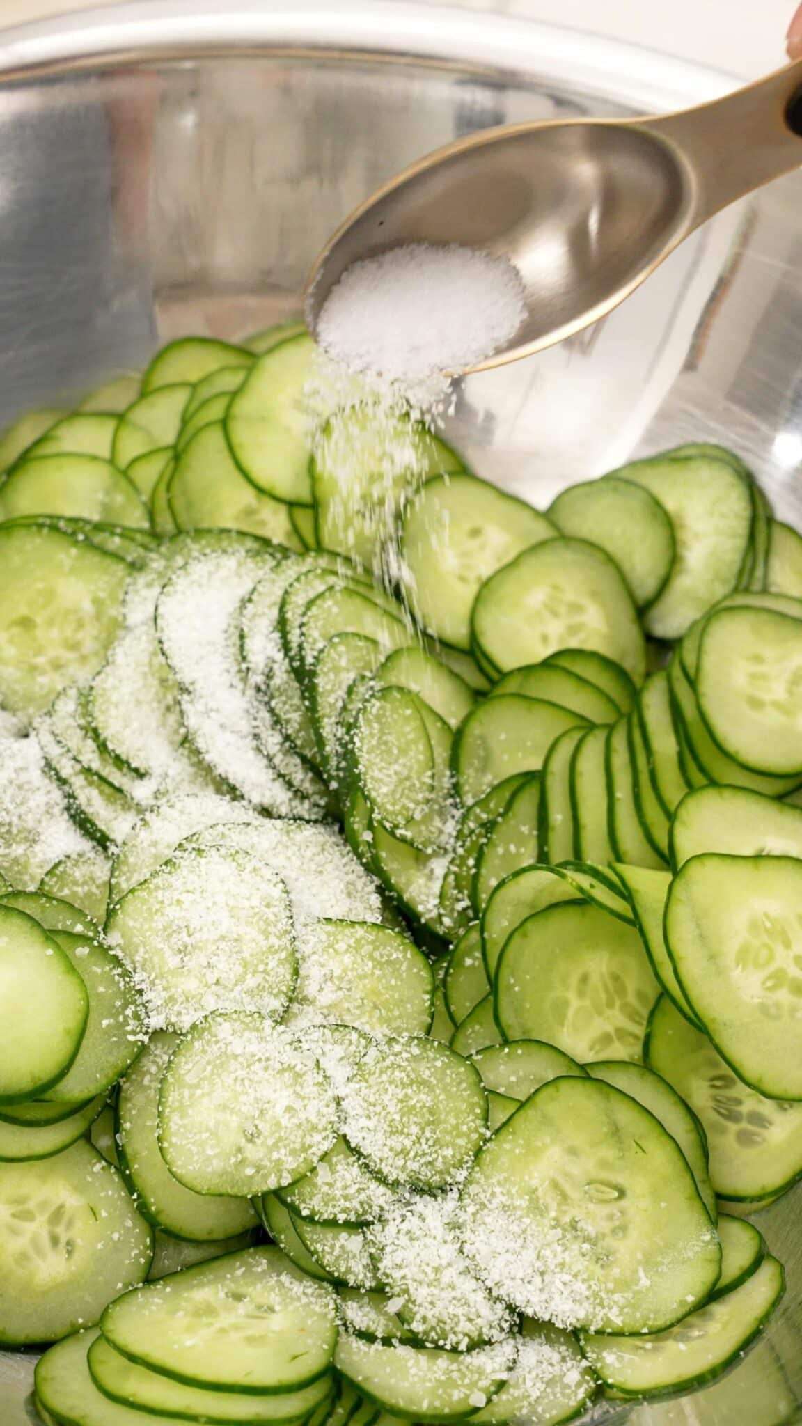 Adding salt to cucumbers in a bowl.