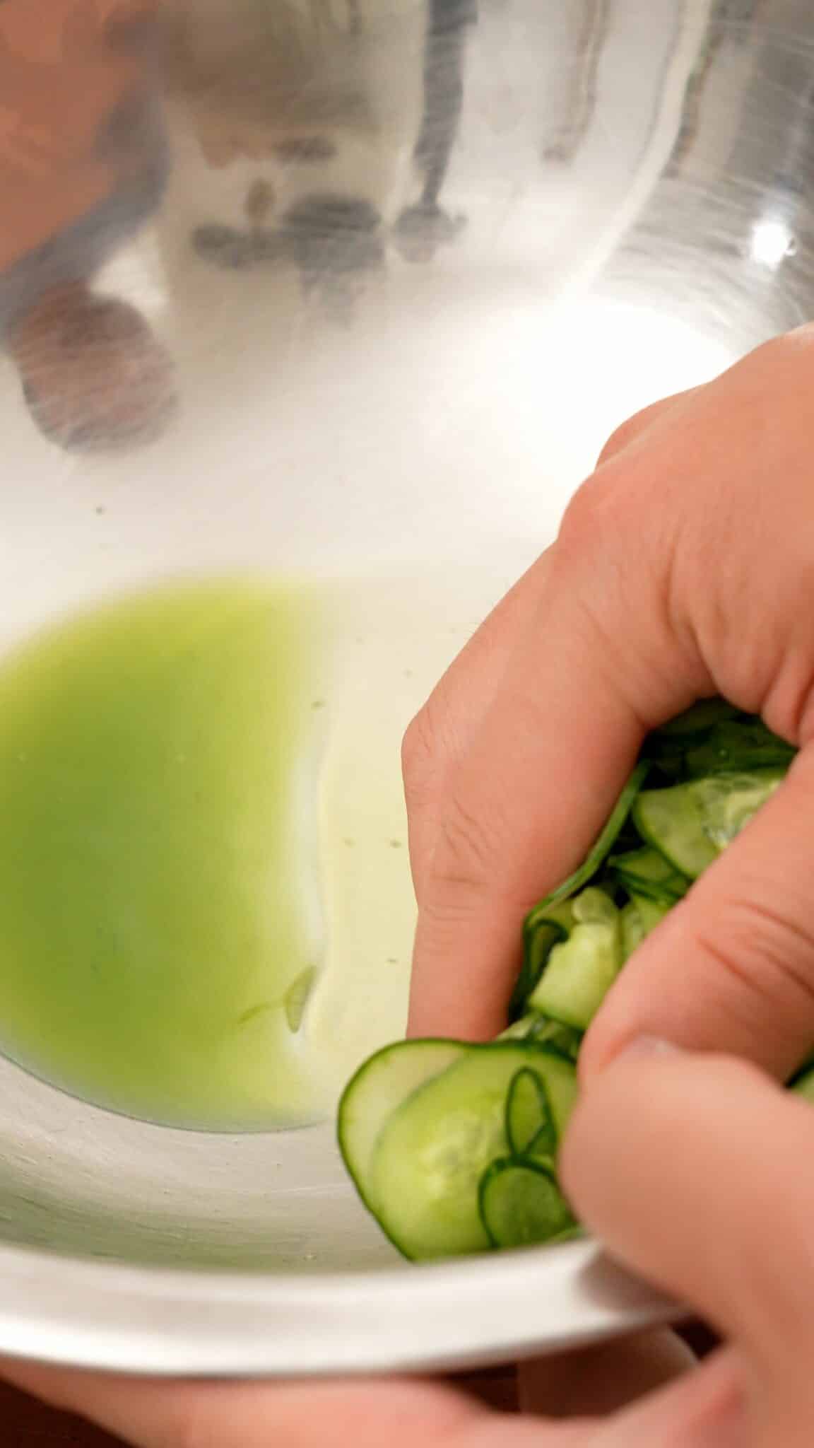 Squeezing water out of salted cucumbers in a bowl.