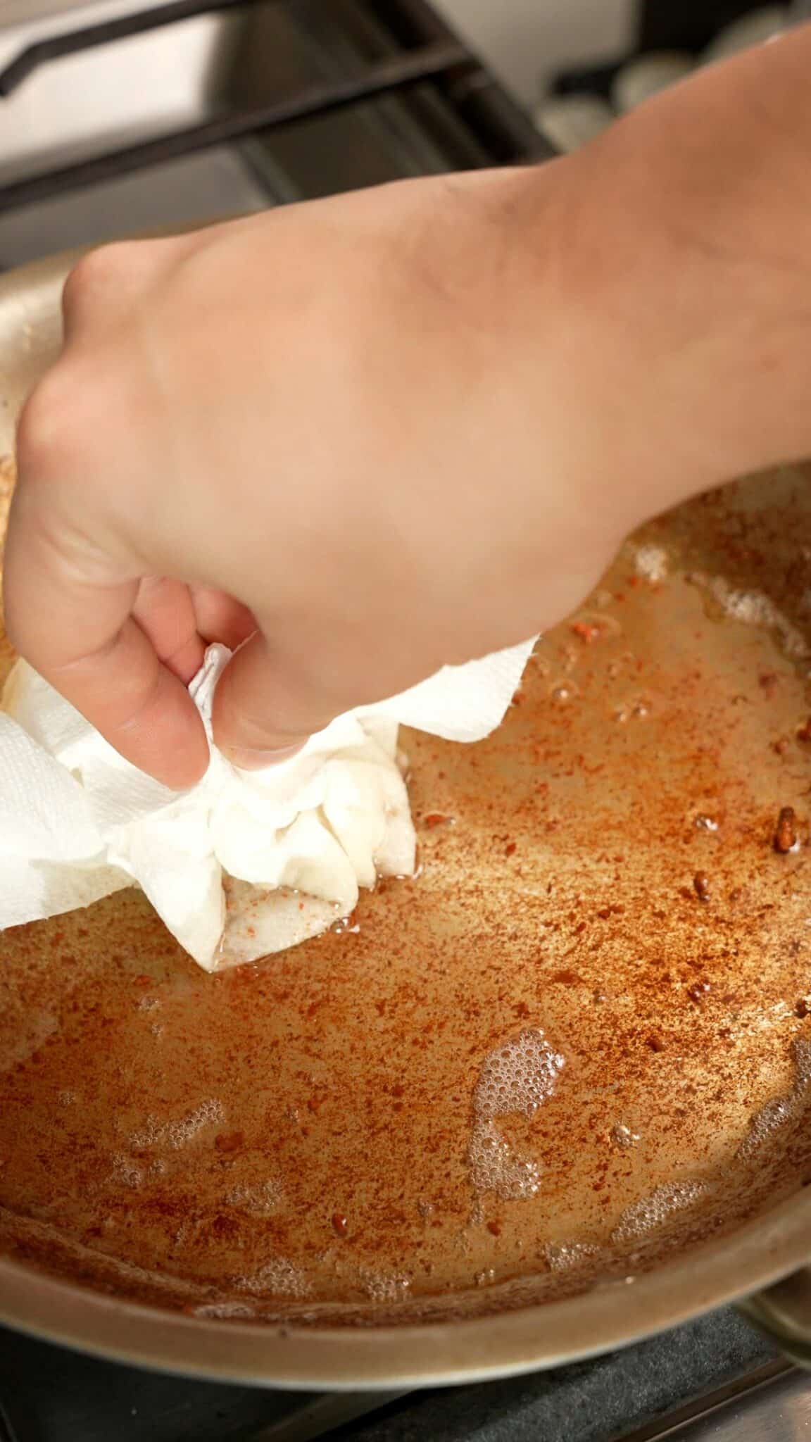 Draining bacon fat with a paper towel in a pan.