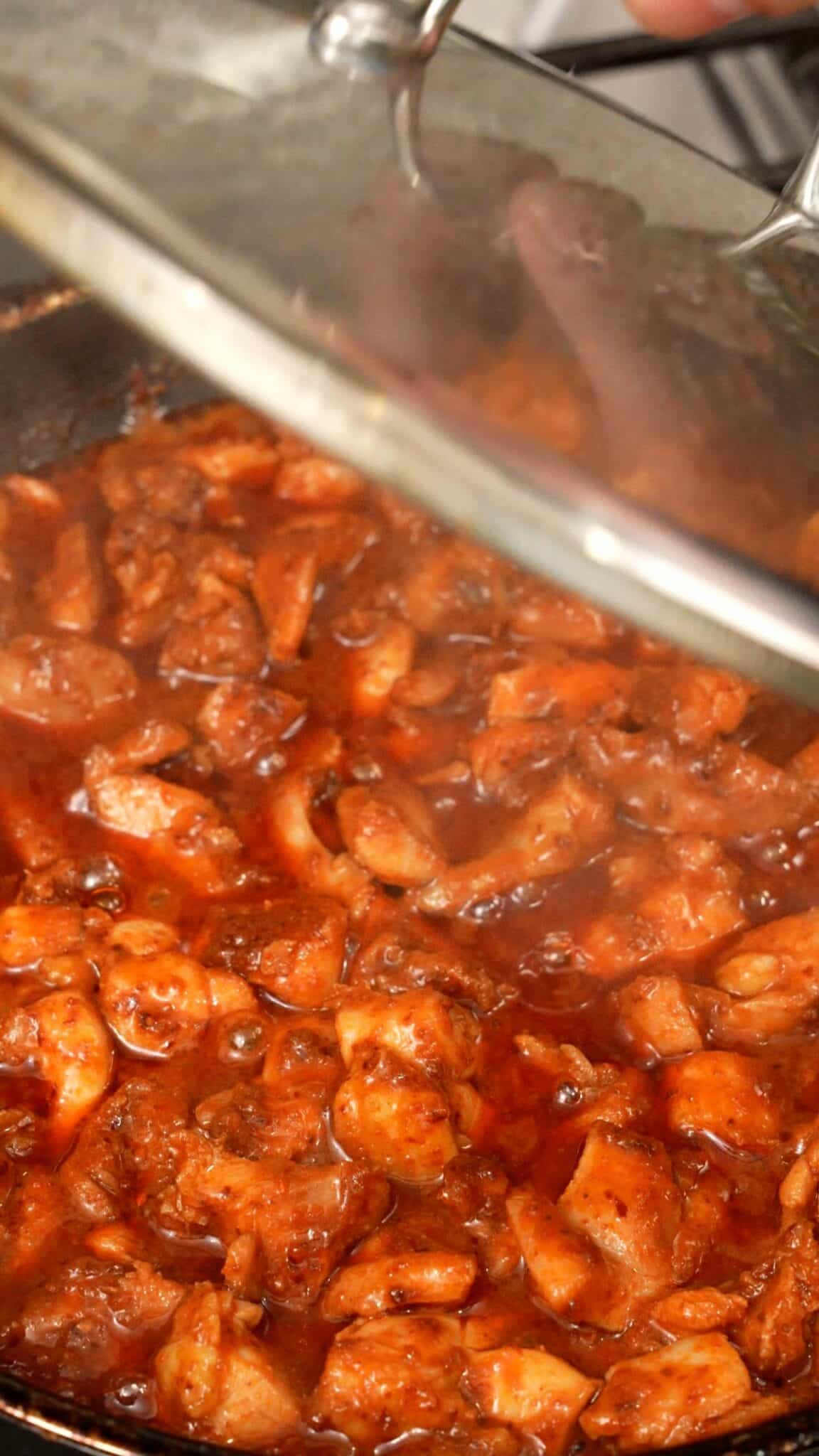 Removing a lid from a pan of Korean fire chicken.