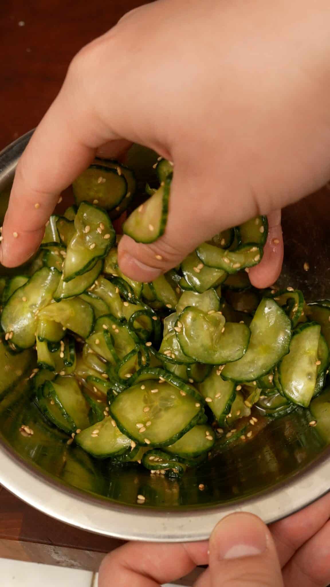 A hand mixing cucumbers and dressing.