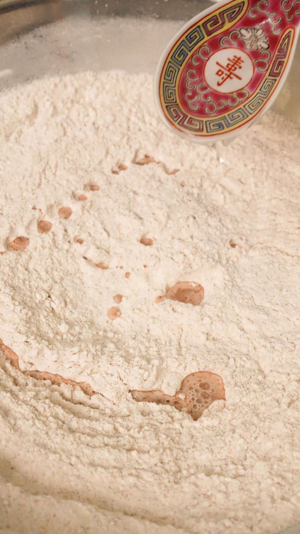 A spoon adding water to the dry batter to make craggily bits.