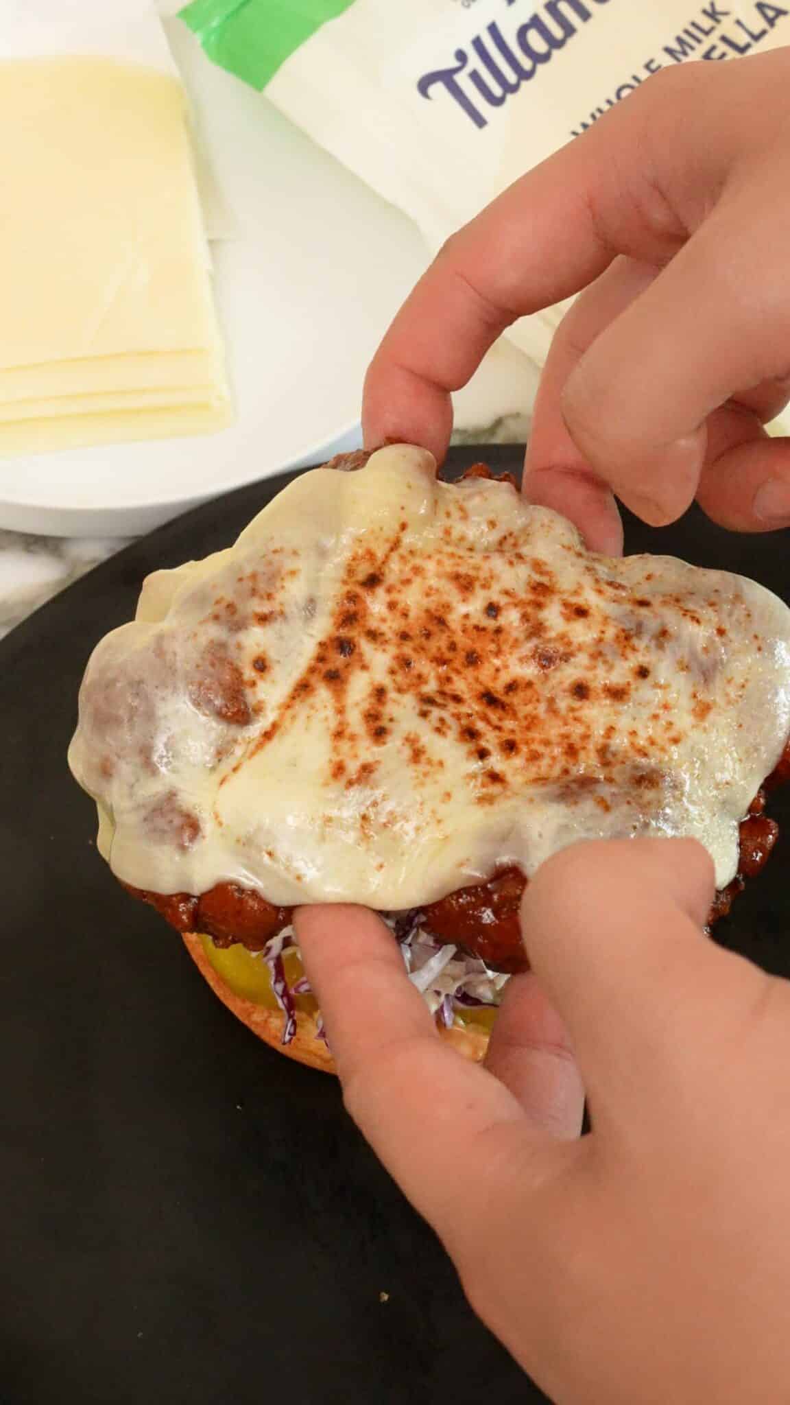 A pair of hands assembling a Korean Fried Chicken Sandwich.