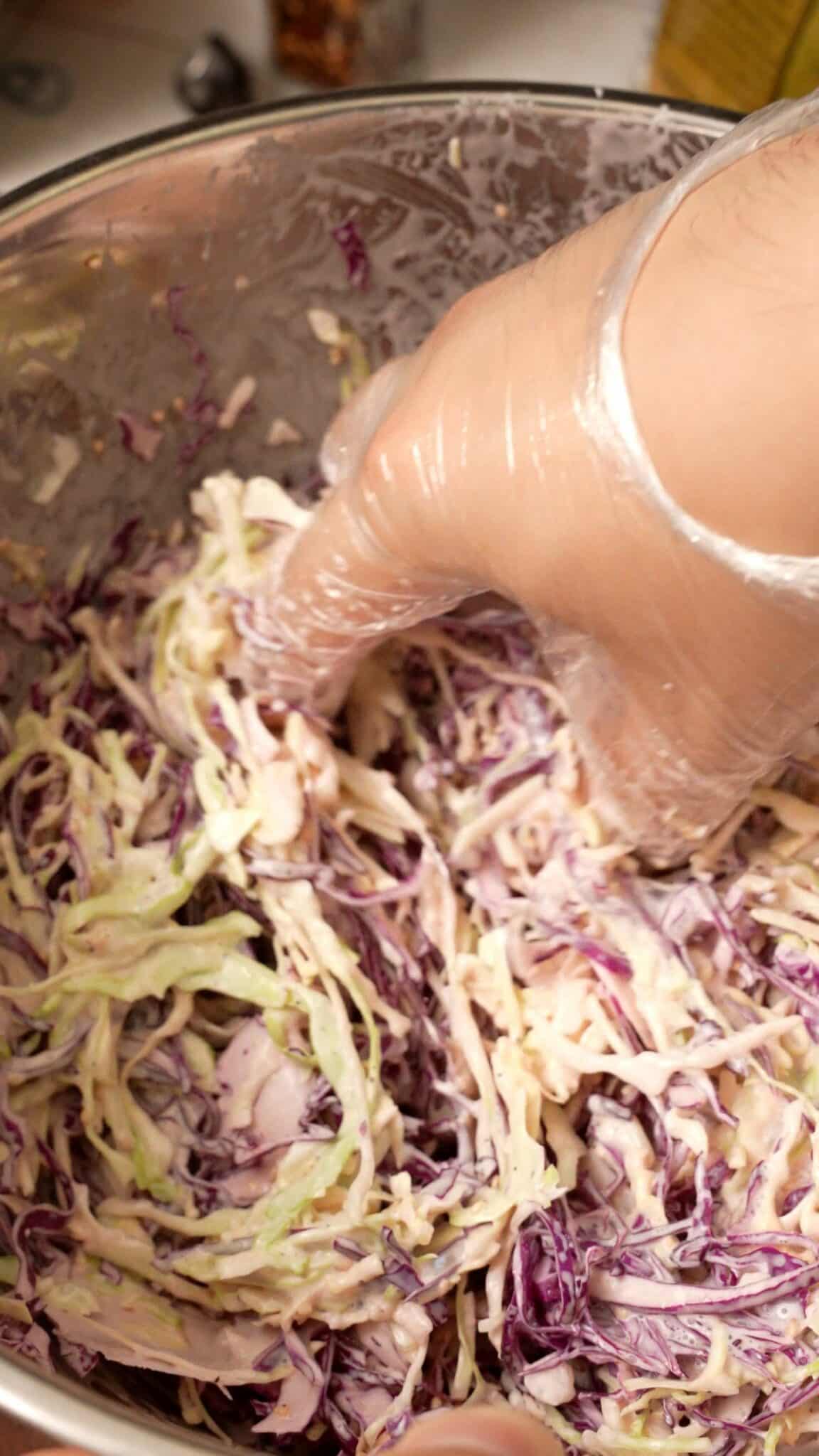 A hand mixing the cabbage slaw in a bowl.