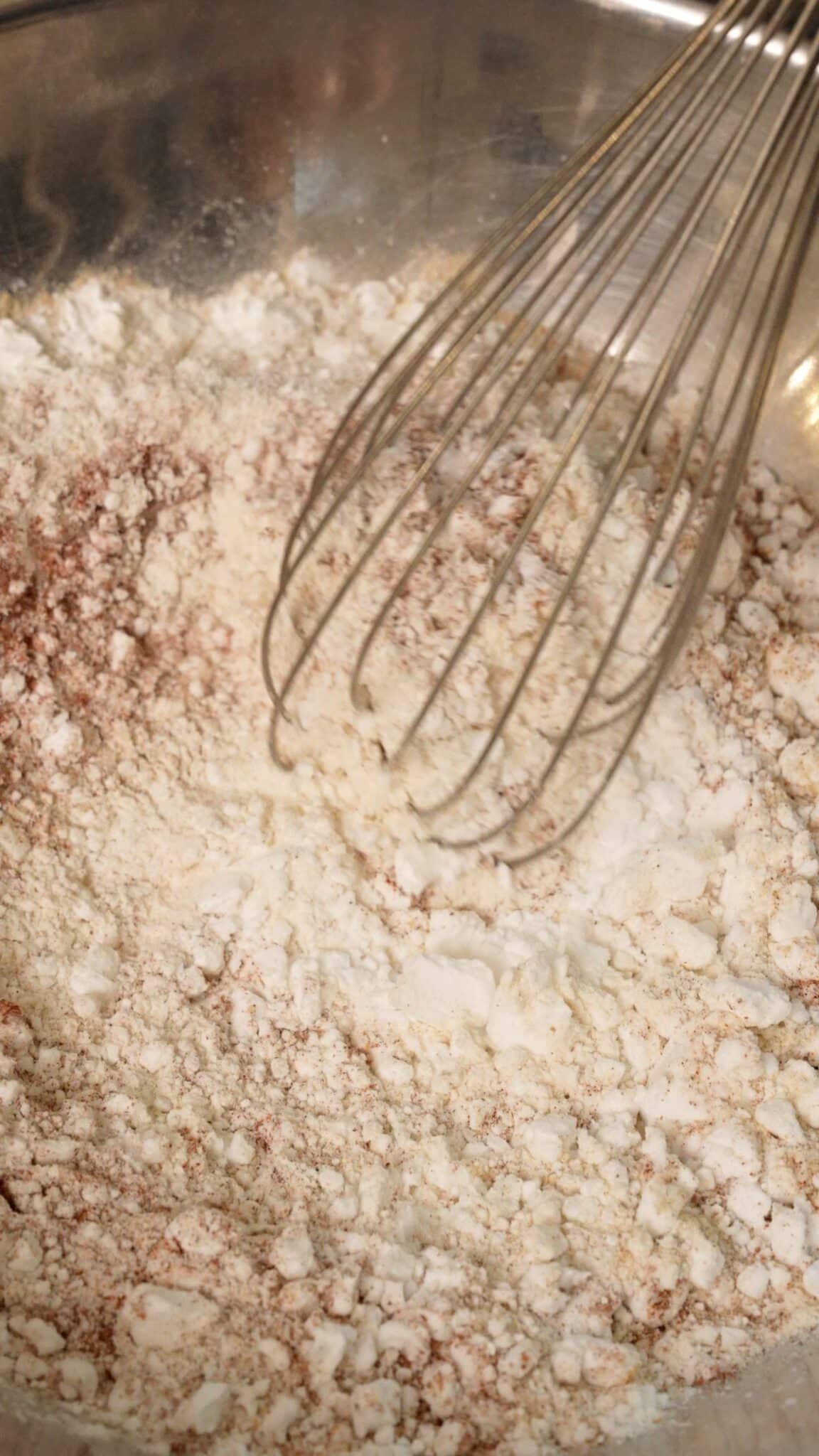 A whisk mixing the dry batter with seasonings.