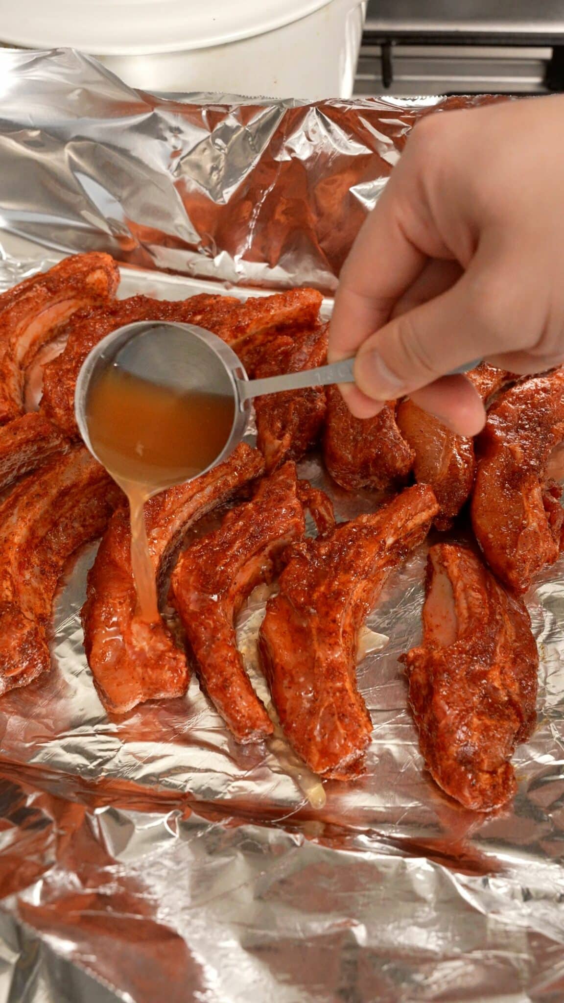 Adding apple cider vinegar on a tray to the oven baked ribs.