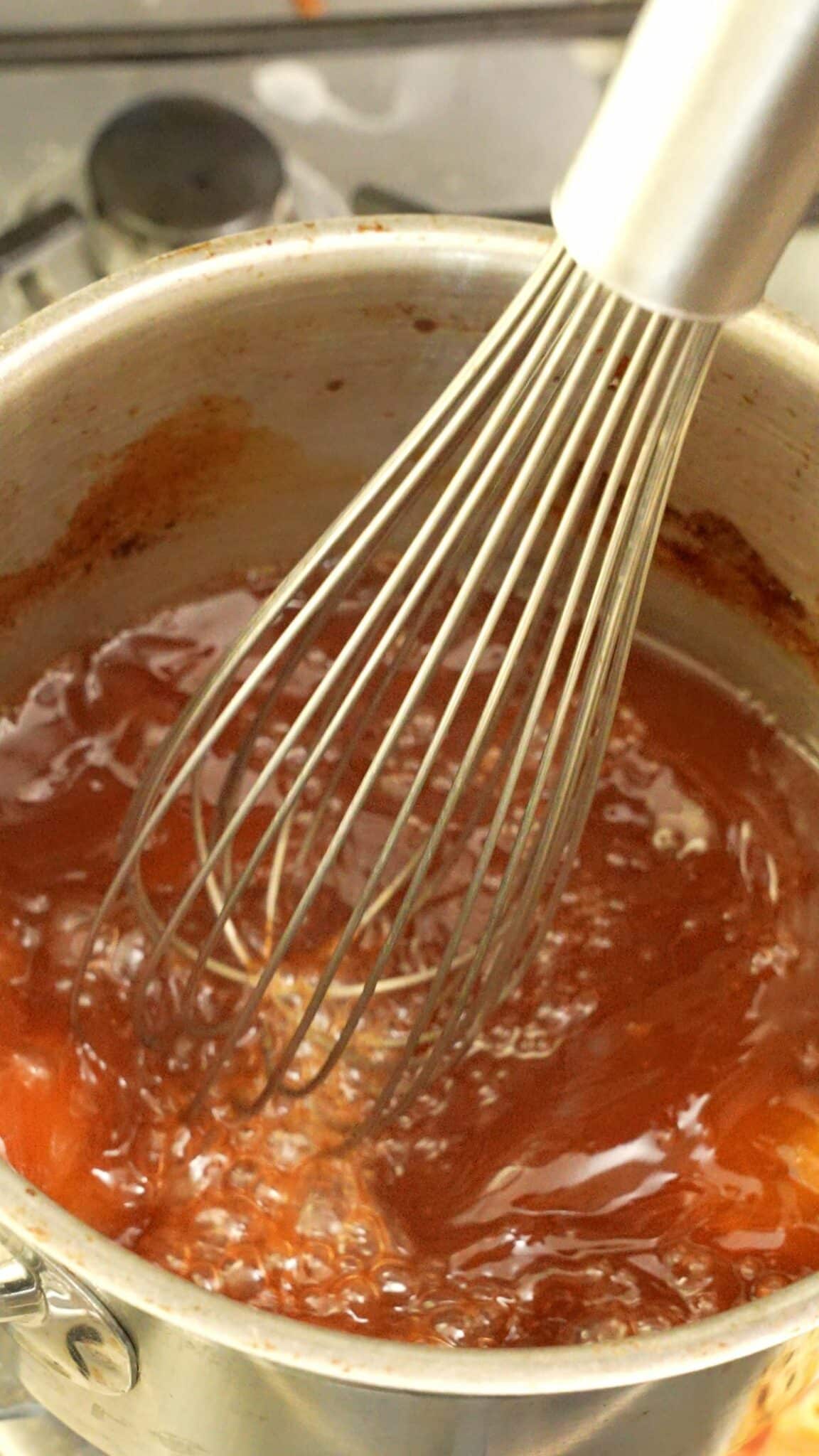 A whisk mixing the sweet and sour sauce ingredients in a pot.