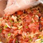 A hand wearing a glove mixing Ahi Tuna Poke in a metal mixing bowl.
