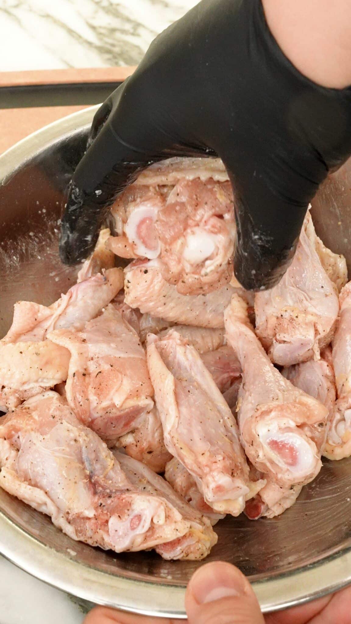 A hand mixing chicken wings with seasonings and baking powder.