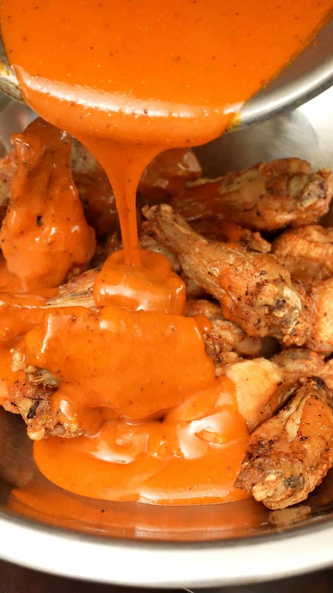 Buffalo sauce being poured on air fryer buffalo wings.