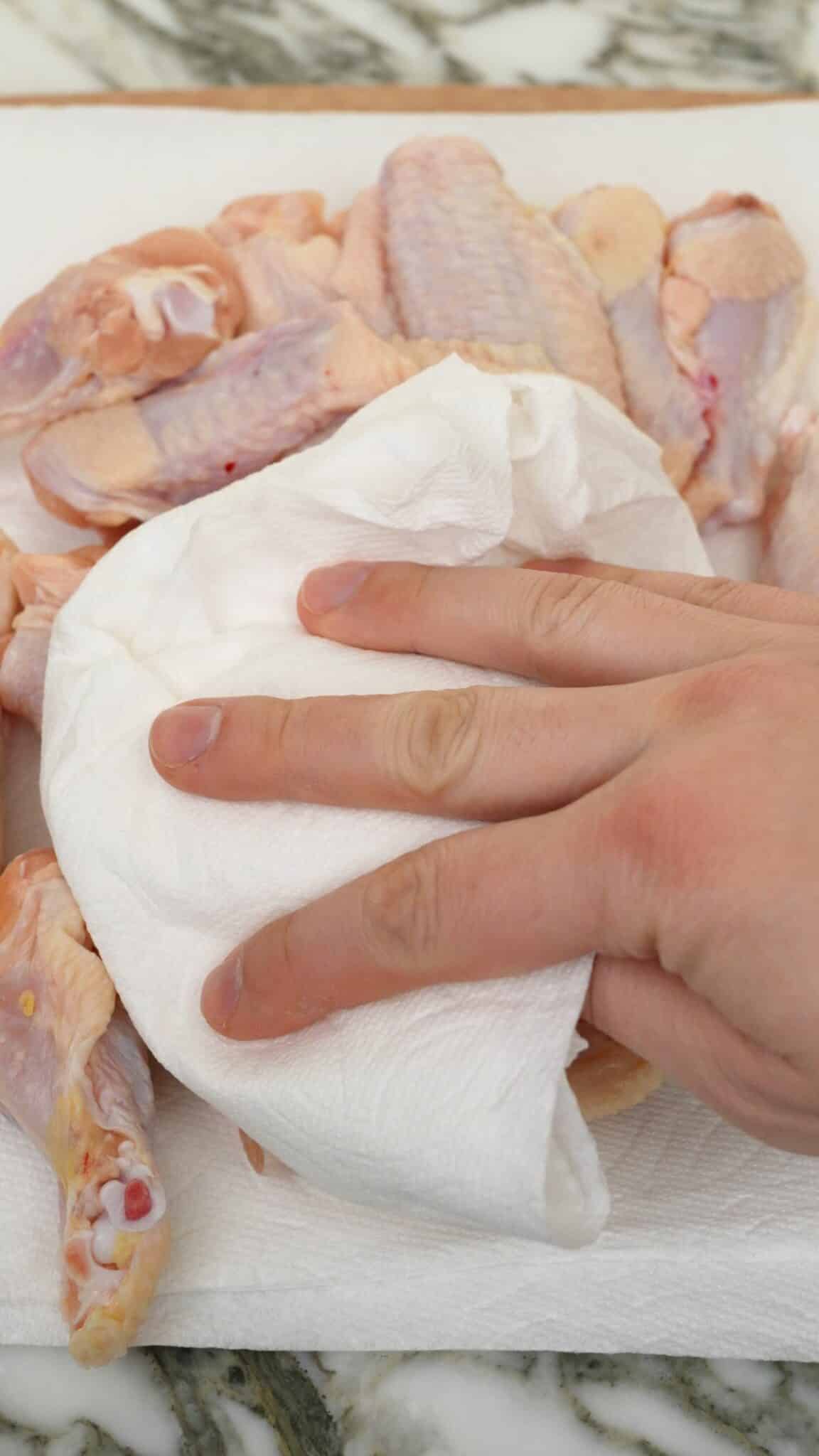 Patting chicken wings dry with a paper towel.