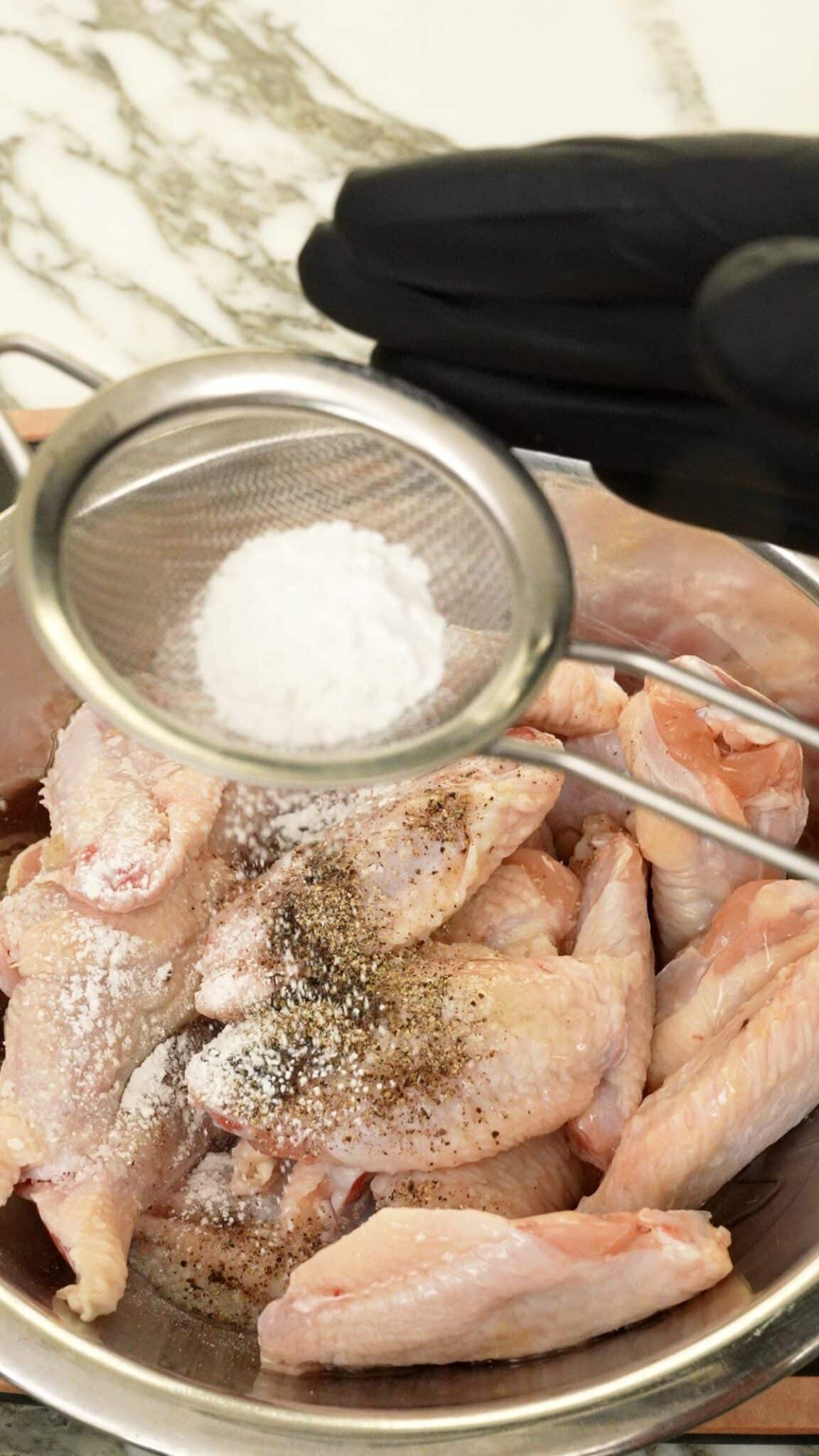 Baking powder sifting over seasoned chicken wings.