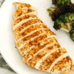 A pan seared chicken breast cut into slices and on a plate with broccoli.