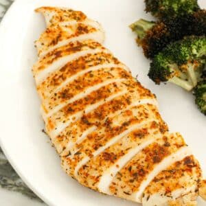 A pan seared chicken breast cut into slices and on a plate with broccoli.