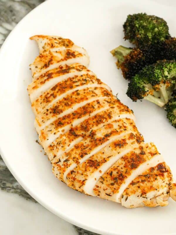A pan seared chicken breast cut into slices and on a plate with broccoli.