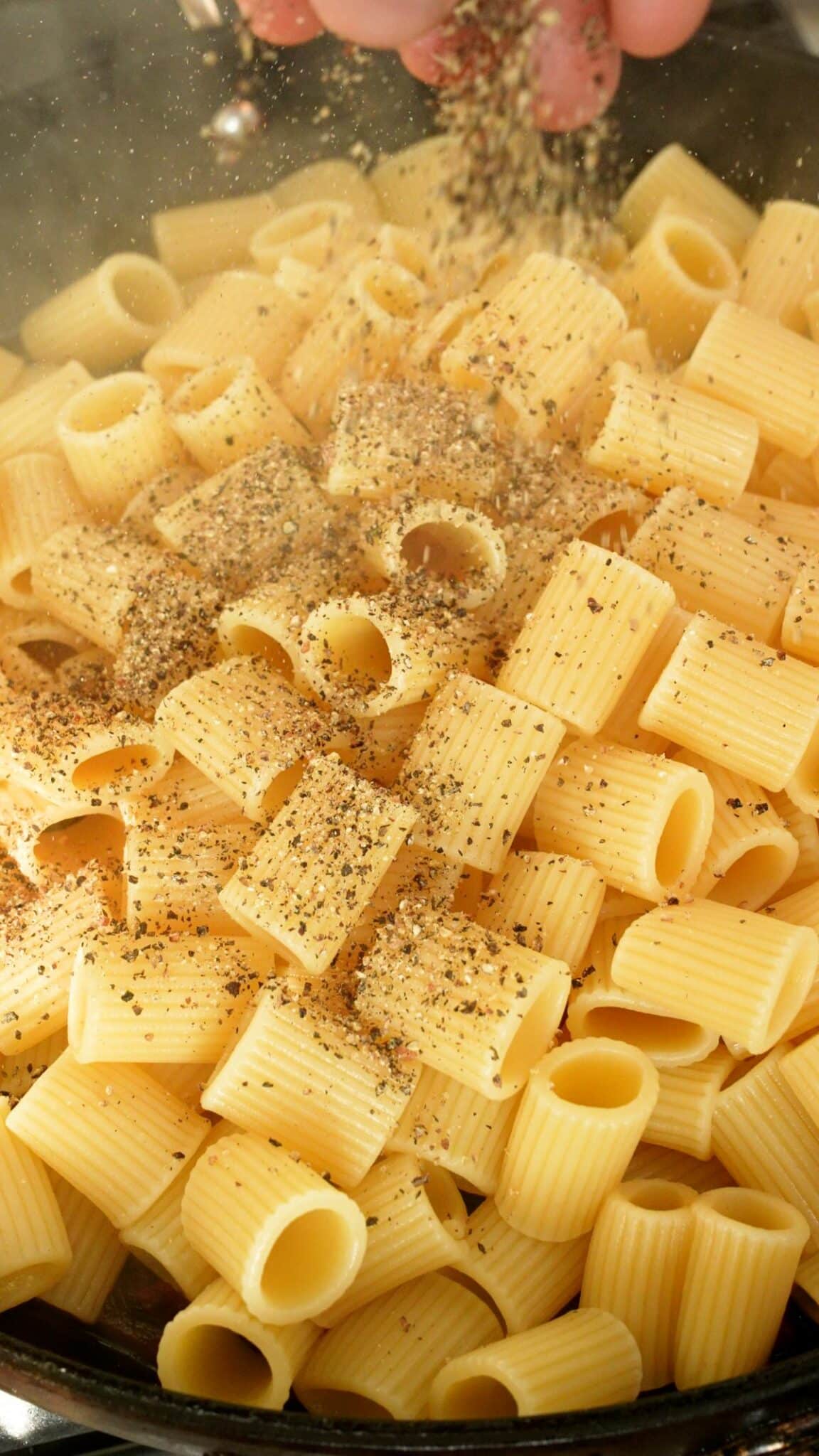 Black pepper being added to mezzi rigatoni.