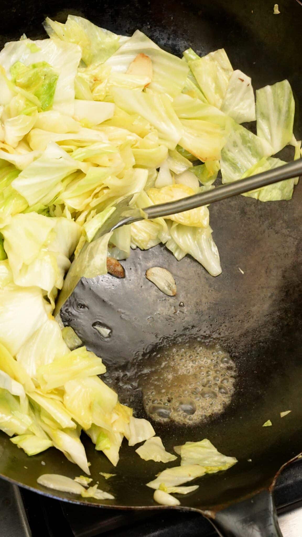 A spatula pushing cabbage in a wok to show water being cooked out.