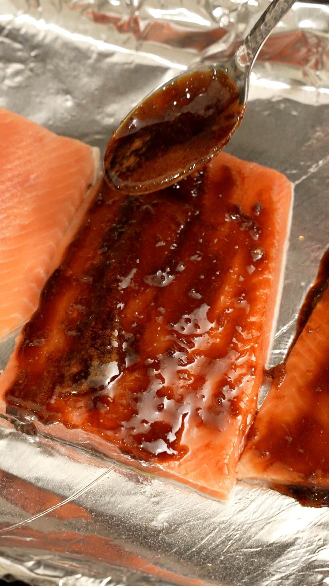 A spoon adding the honey soy glaze onto the raw salmon.