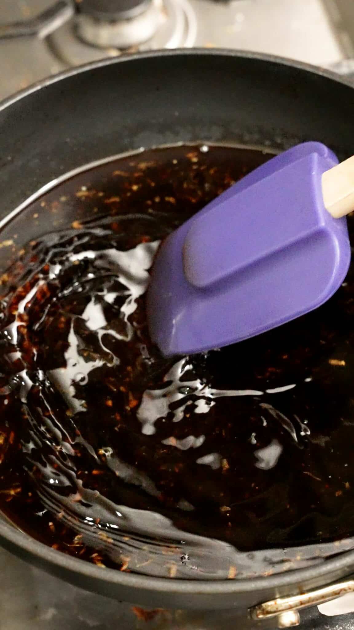 A spatula mixing the honey soy glaze in a pan.