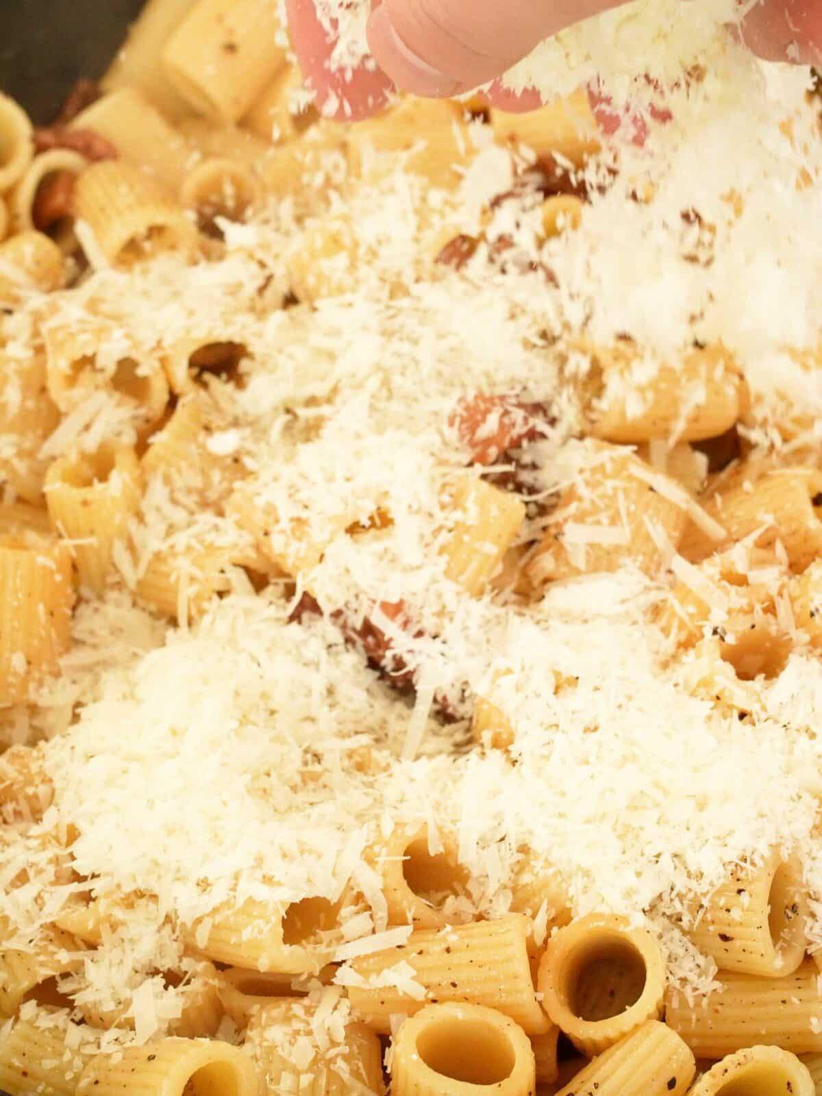 Parmesan cheese being added to a pan of pasta.