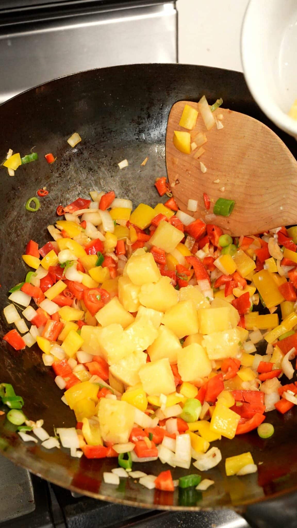 Fresh pineapple added to a wok with vegetables.