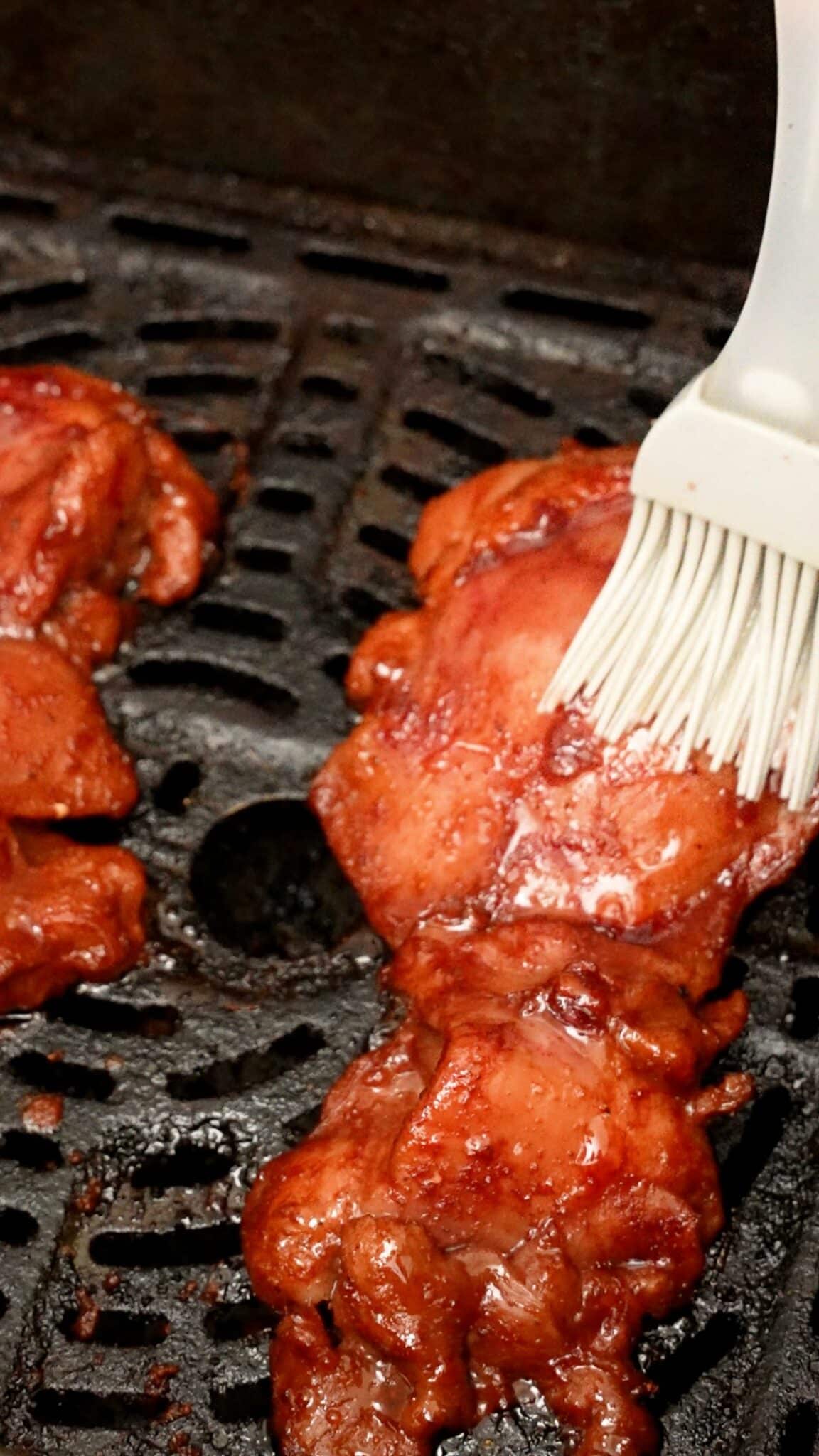 Marinated chicken thigh in the air fryer being basted with glaze.