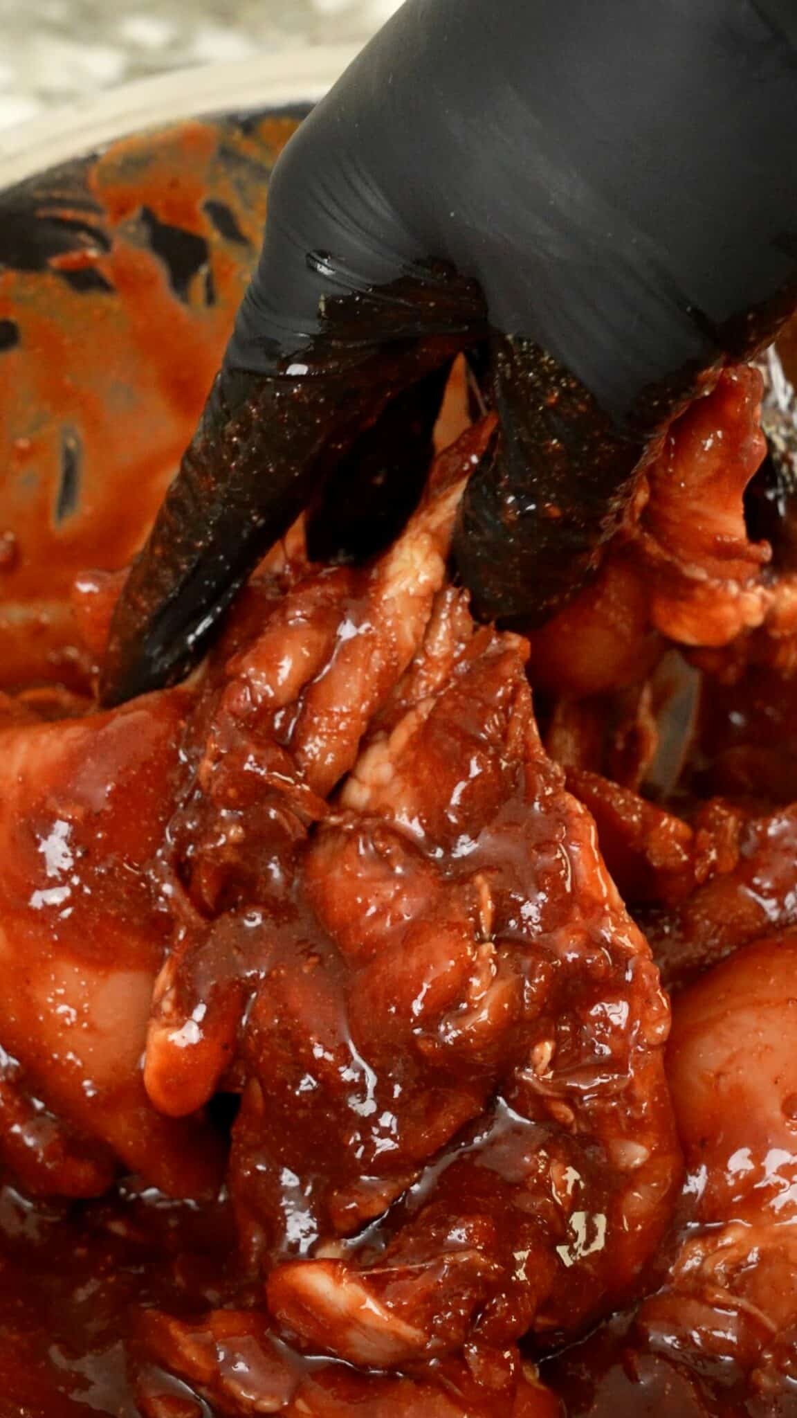 A hand mixing chicken thigh in the char siu marinade.