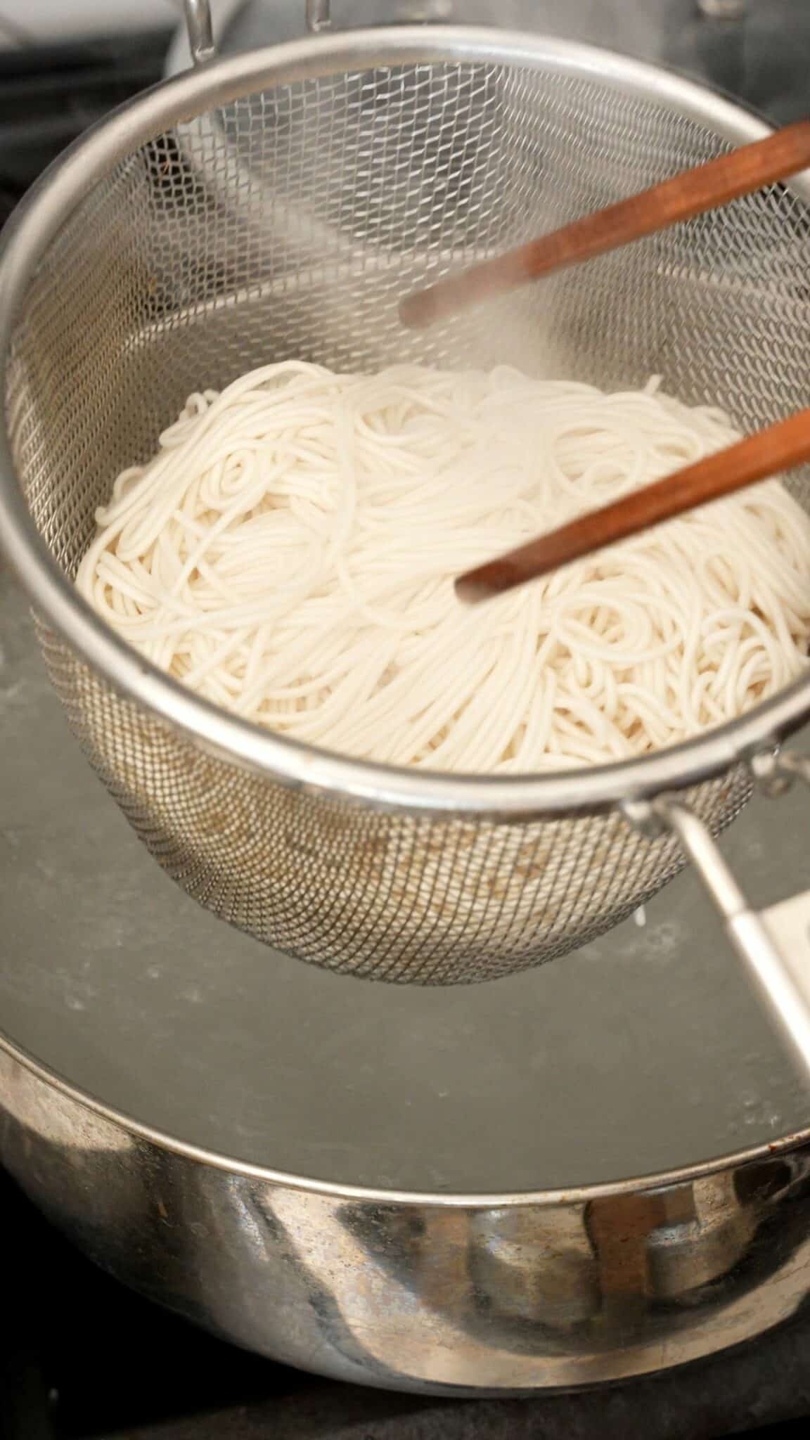 Cooked noodles being strained from the pot of water.