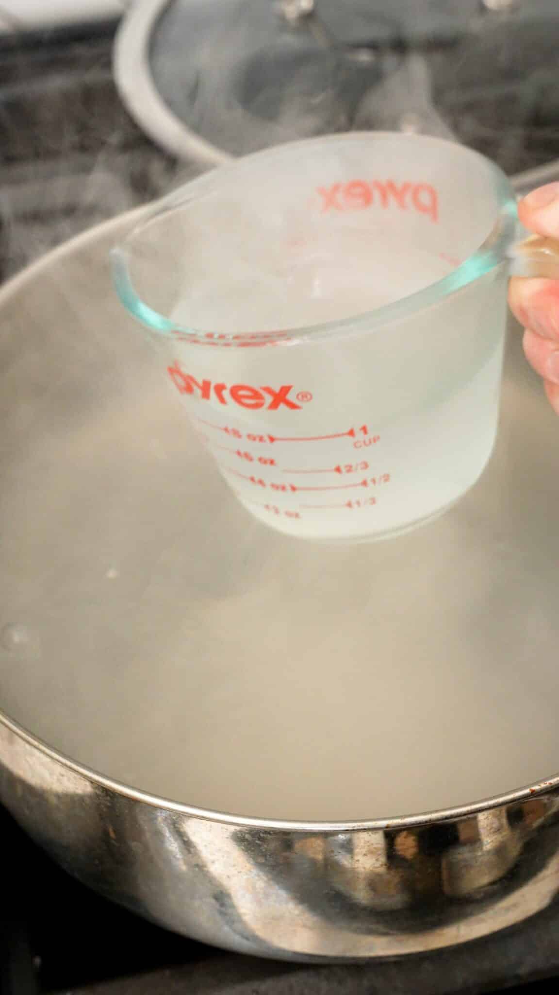 A measuring cup reserving a cup of cooking water from the pot.