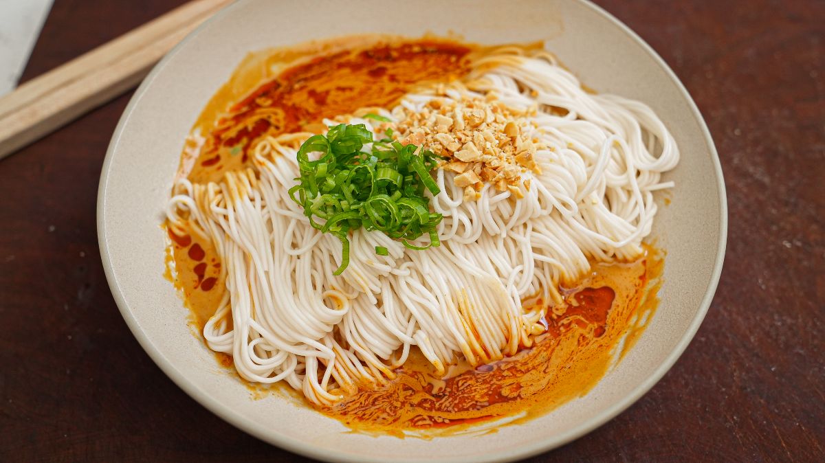 Din Tai Fung Noodles in a bowl with the sesame sauce garnished with scallions and crushed peanuts.