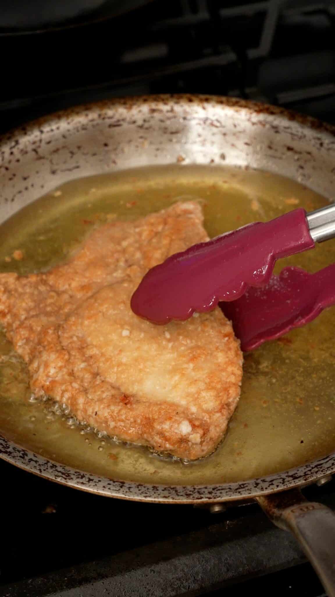 Pork chops frying in oil in a pan.
