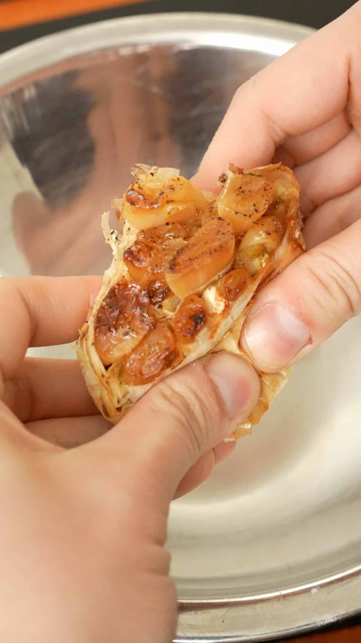 A roasted head of garlic being held by two hands.