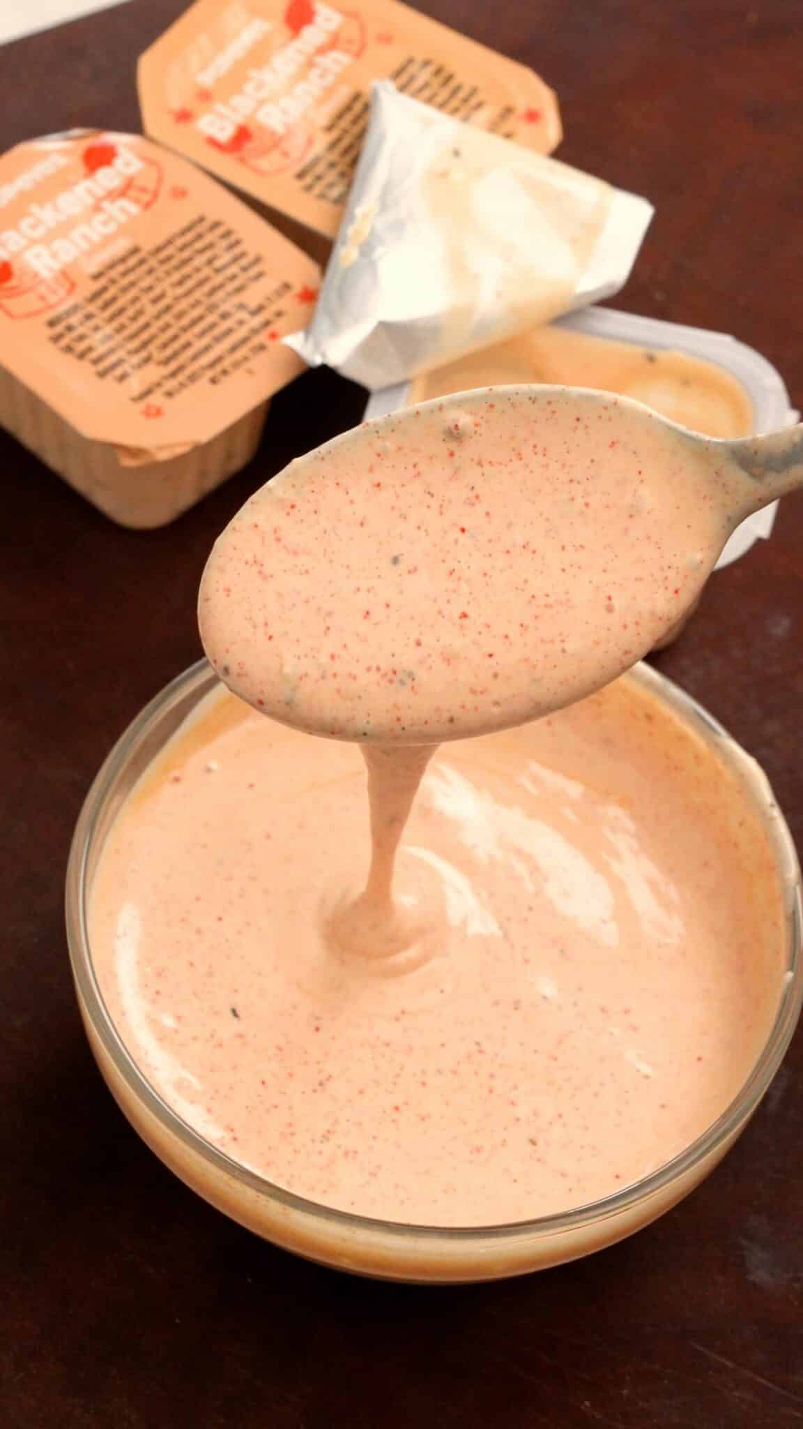 A spoon with a small bowl of copycat Popeyes blackened ranch.