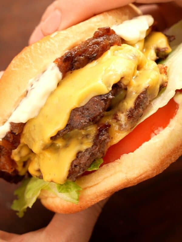 Smash Burger constructed with tomato, lettuce, beef patties, american cheese, carmelized onions, and mayo on a brioche bun.
