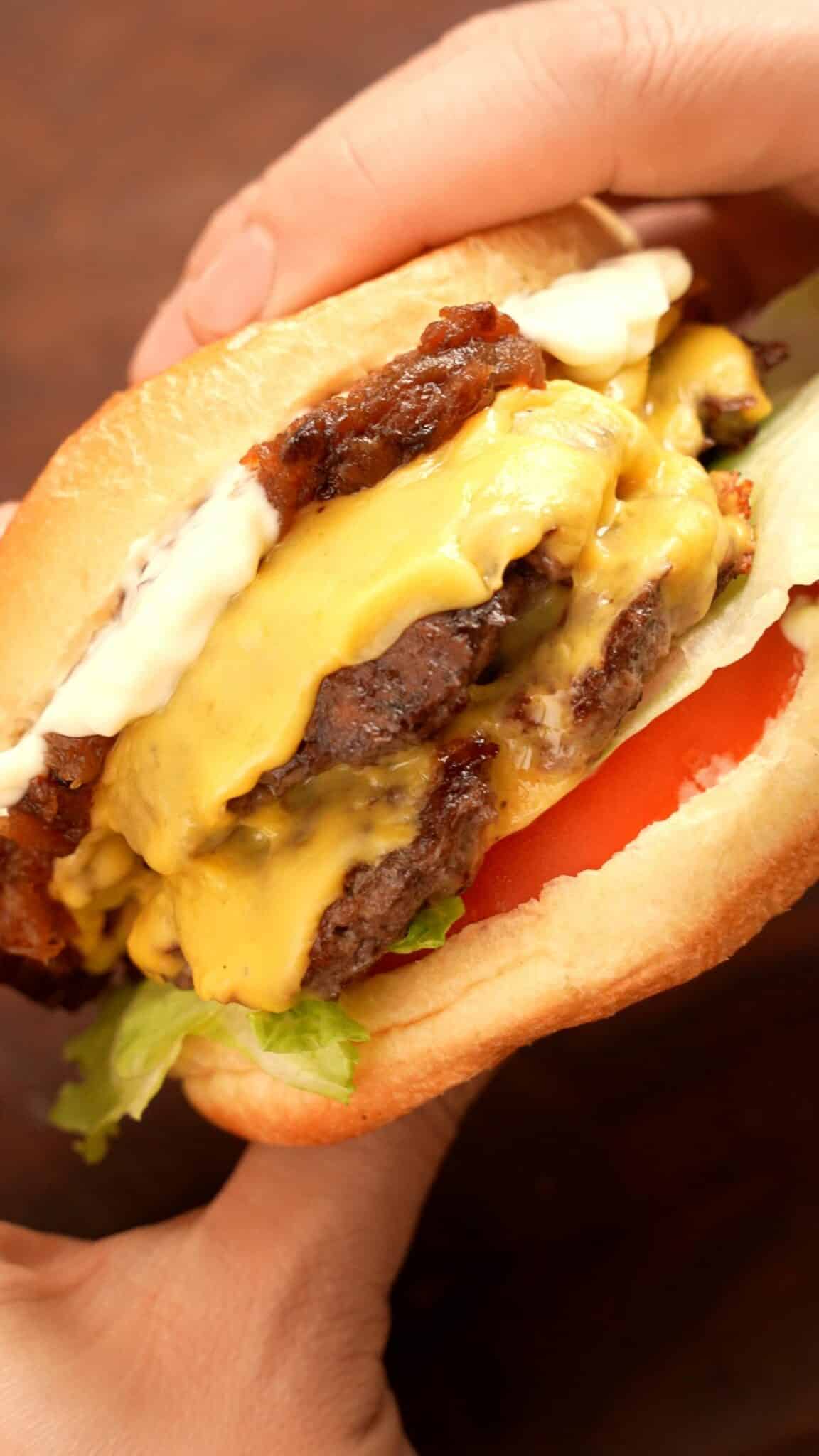 Smash Burger constructed with tomato, lettuce, beef patties, american cheese, carmelized onions, and mayo on a brioche bun.