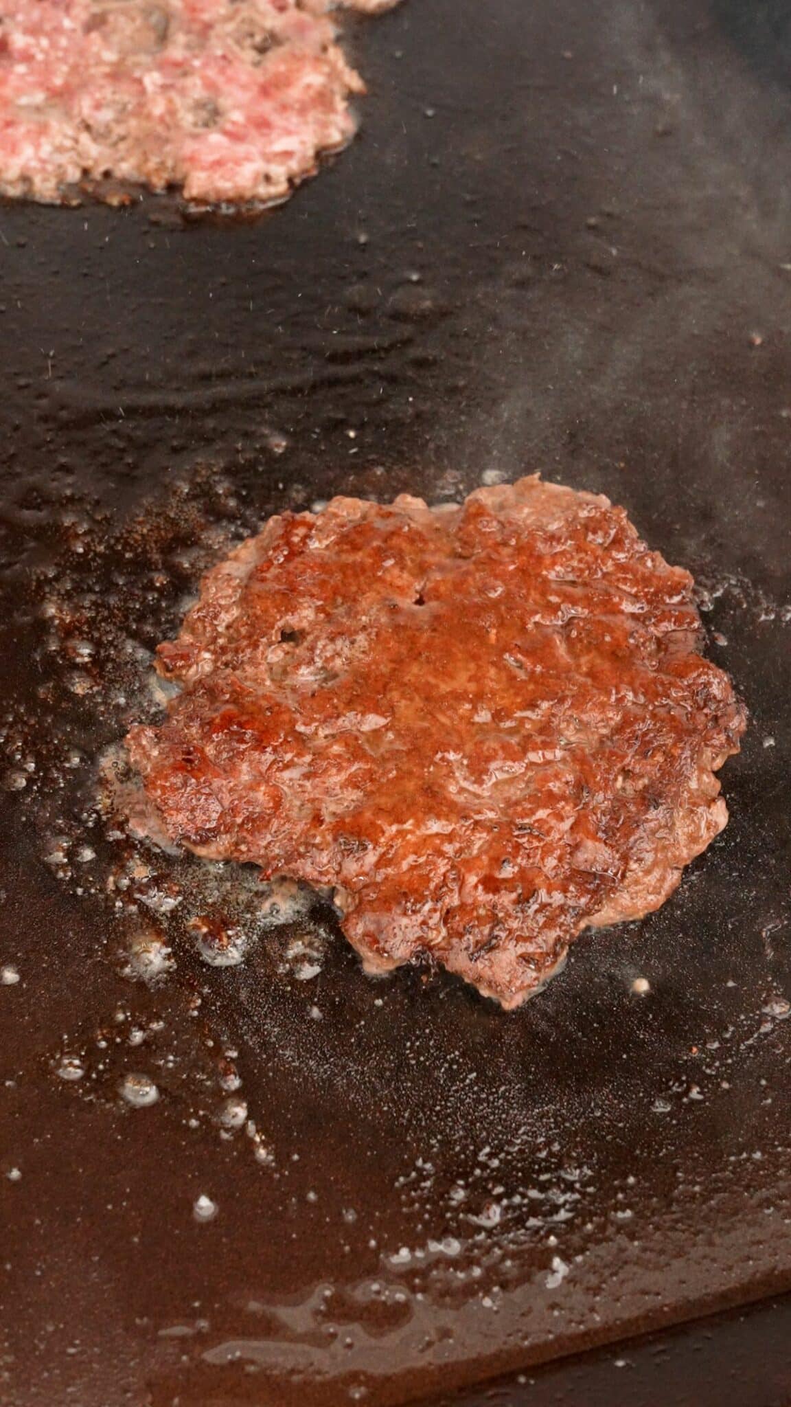 A cooked burger patty on a griddle.