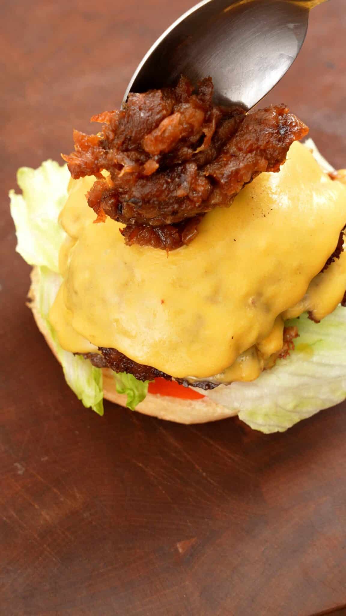 Carmelized onions being added to the smash burger with tomato and lettuce.