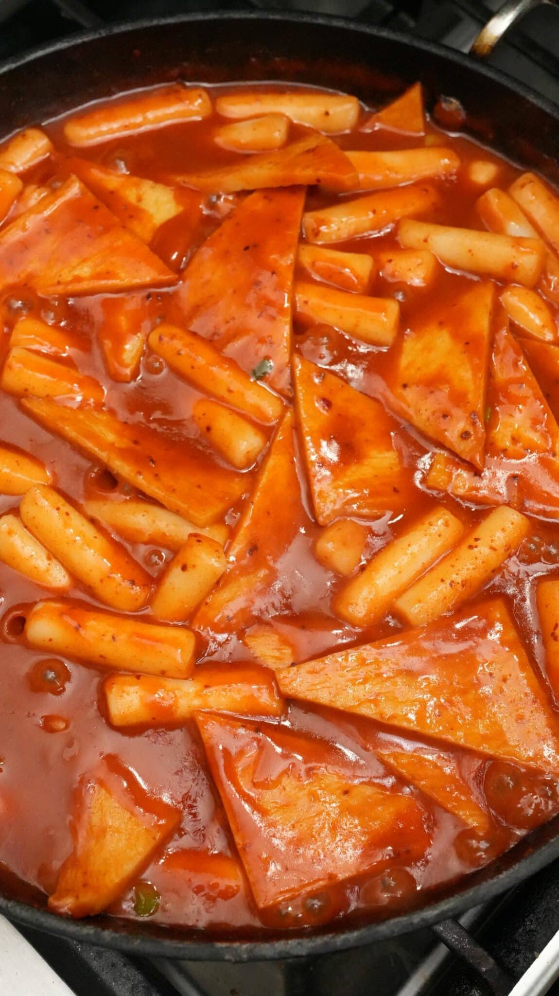 Tteokbokki simmering in a pan with fish cakes.