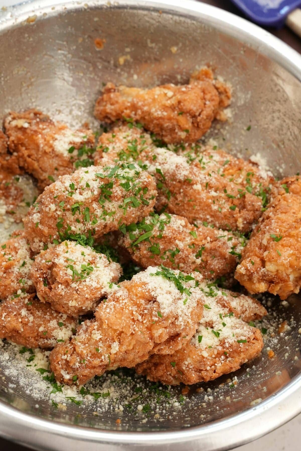 Garlic parmesan wings in a bowl with garlic butter, parmesan cheese, and parsley.