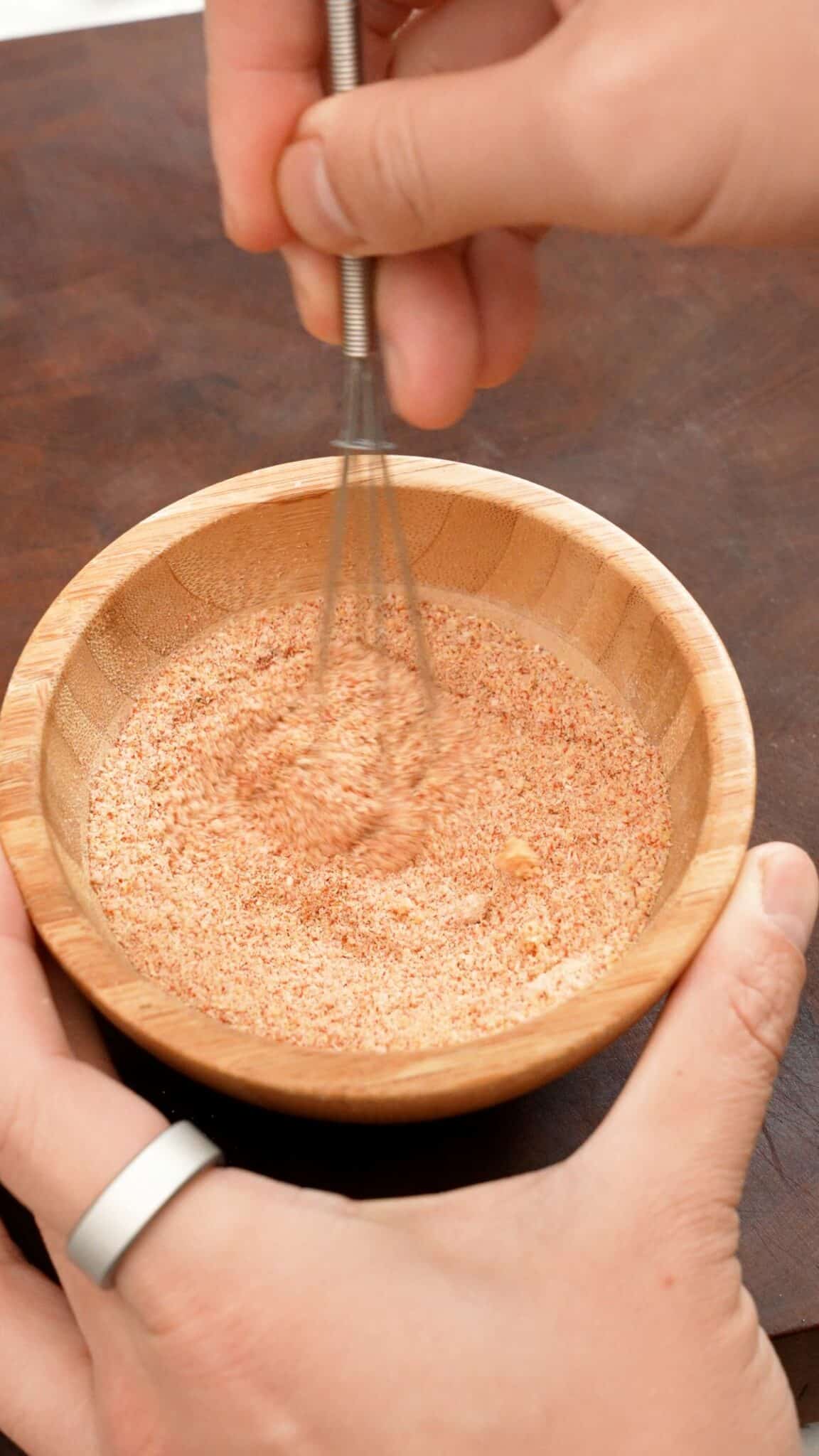 Whisking seasonings in a small wooden bowl with a small whisk.