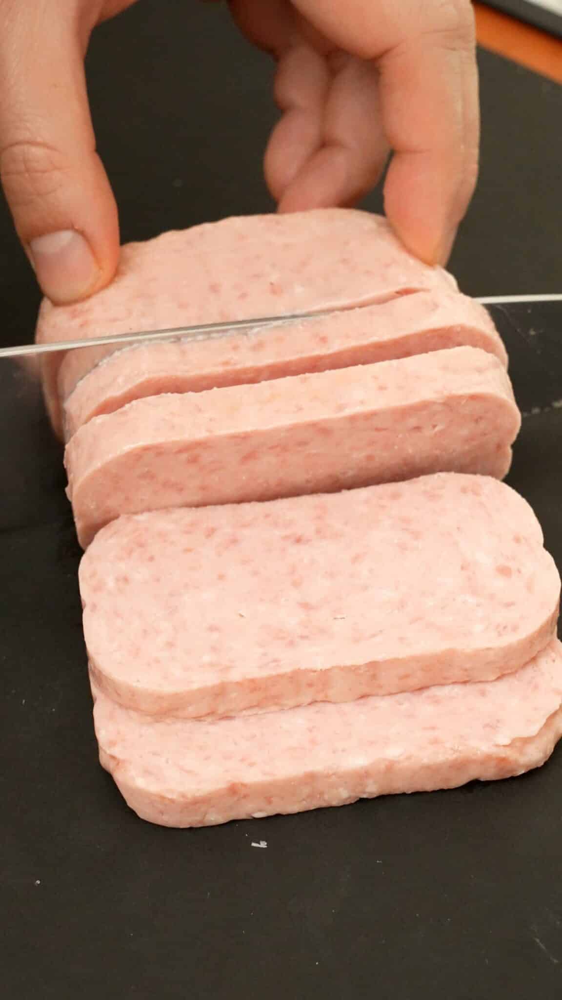 A knife slicing spam into 1/2 inch slices.