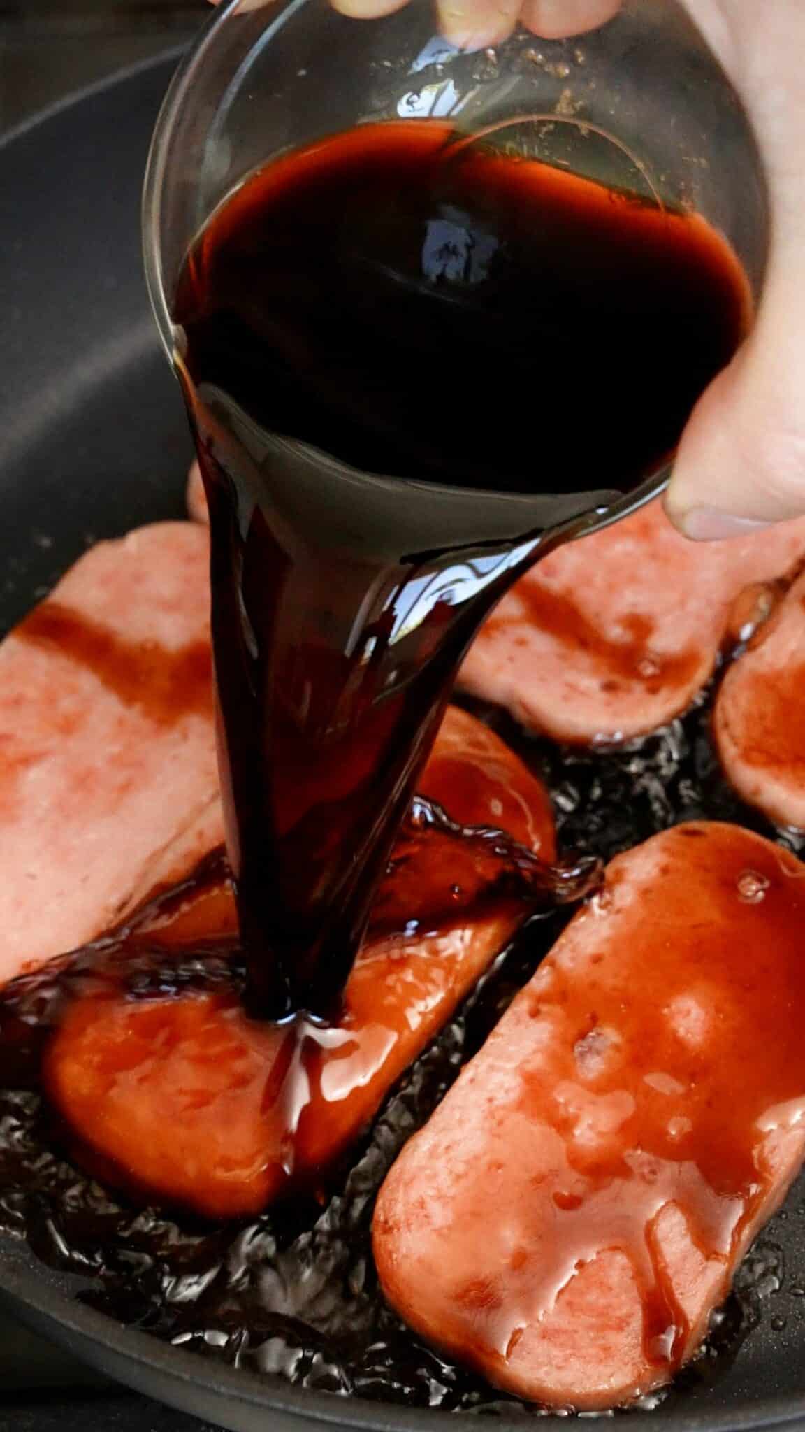 Pouring a mixture of soy sauce, mirin, and brown sugar in a pan with spam.
