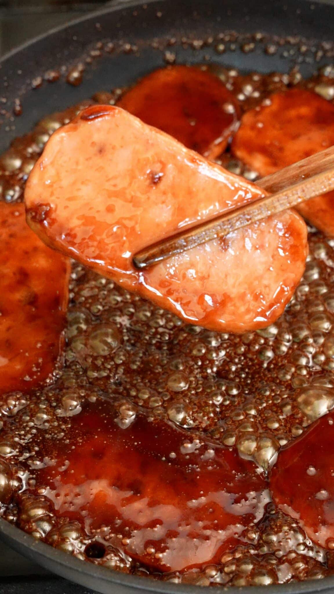 A cooked piece of spam in the soy sauce glaze in a pan.