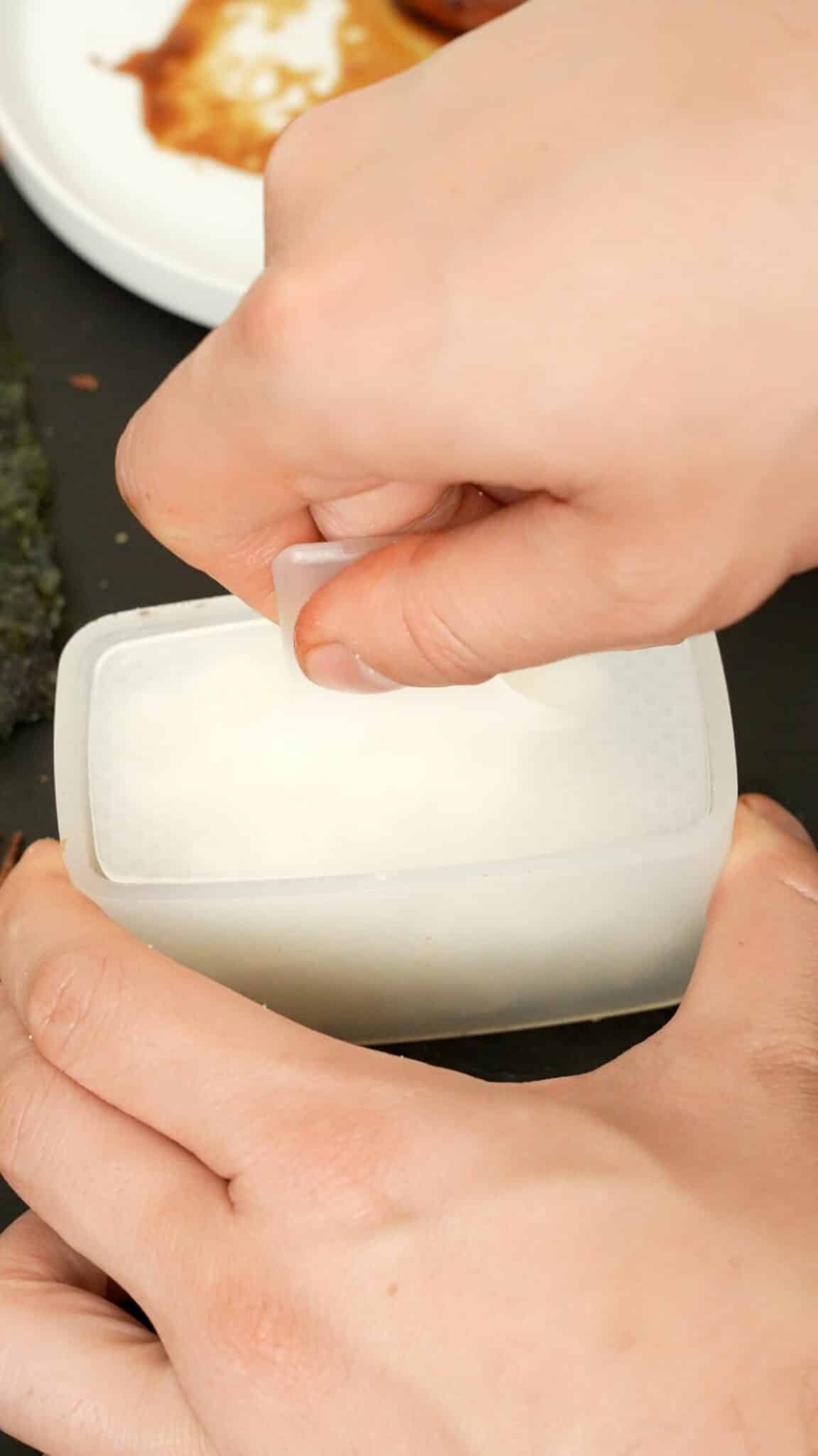 A hand using a musubi mold to press the rice.
